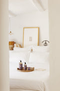 Bedroom with white bedding and a tray with bottles on a nightstand.
