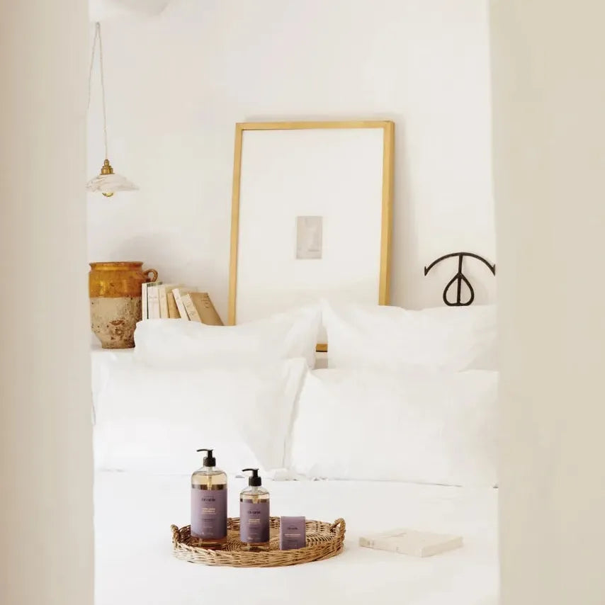 Bedroom with white bedding and a tray with bottles on a nightstand.