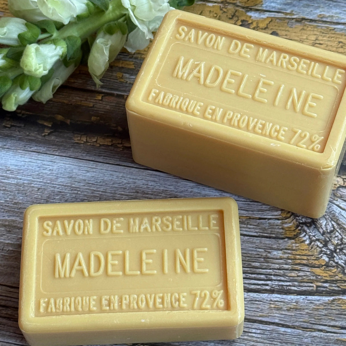 Two bars of Madeleine Marseille soap on a wooden surface with a sprig of lavender.