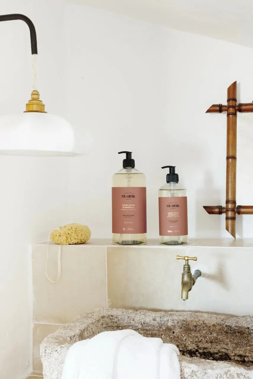 Bathroom setting with bottles on a shelf, faucet, and bath mat.