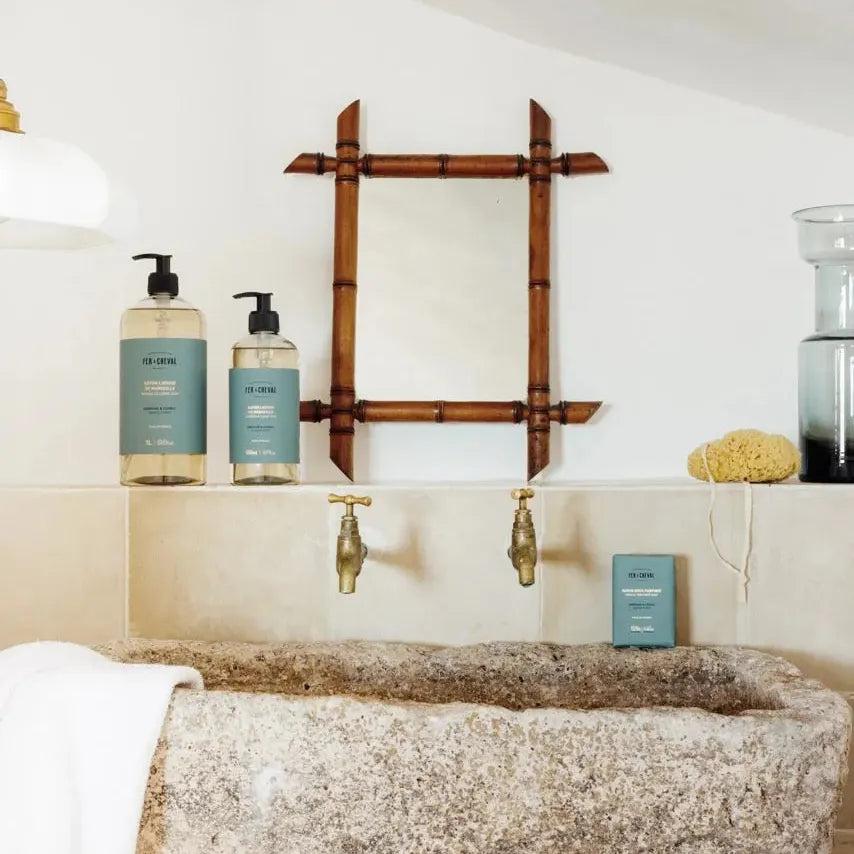 Bathroom setting with stone sink, bamboo mirror, and skincare products.