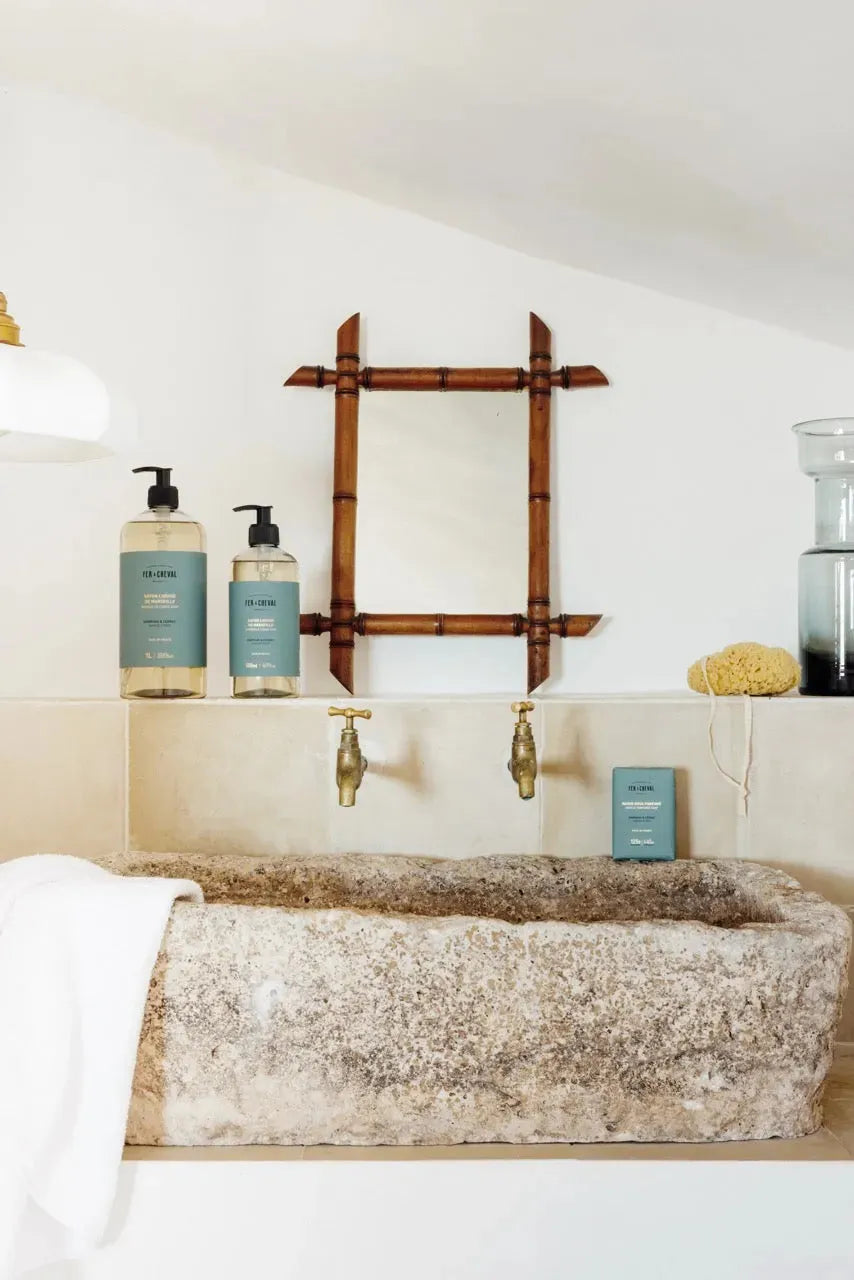 Bathroom setting with stone sink, bamboo mirror, and skincare products.