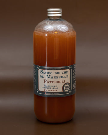 A clear plastic bottle containing orange liquid soap, labeled 'Savon bouche de Marseille Patchouli' with additional text indicating the size and fragrance.