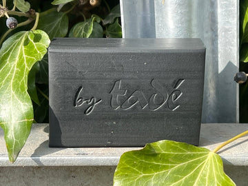 Charcoal Aleppo Soap Bar with green leaves and a factory background