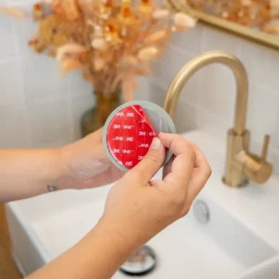 Person holding a red and gray circular object near a sink with a gold faucet.