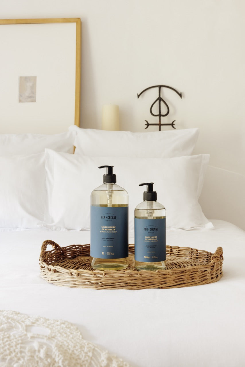 Two bottles of 'Cle de Peau' skincare products on a wicker tray in front of a bed.