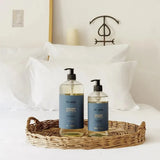 Two bottles of 'Cle de Peau' skincare products on a wicker tray in front of a bed.