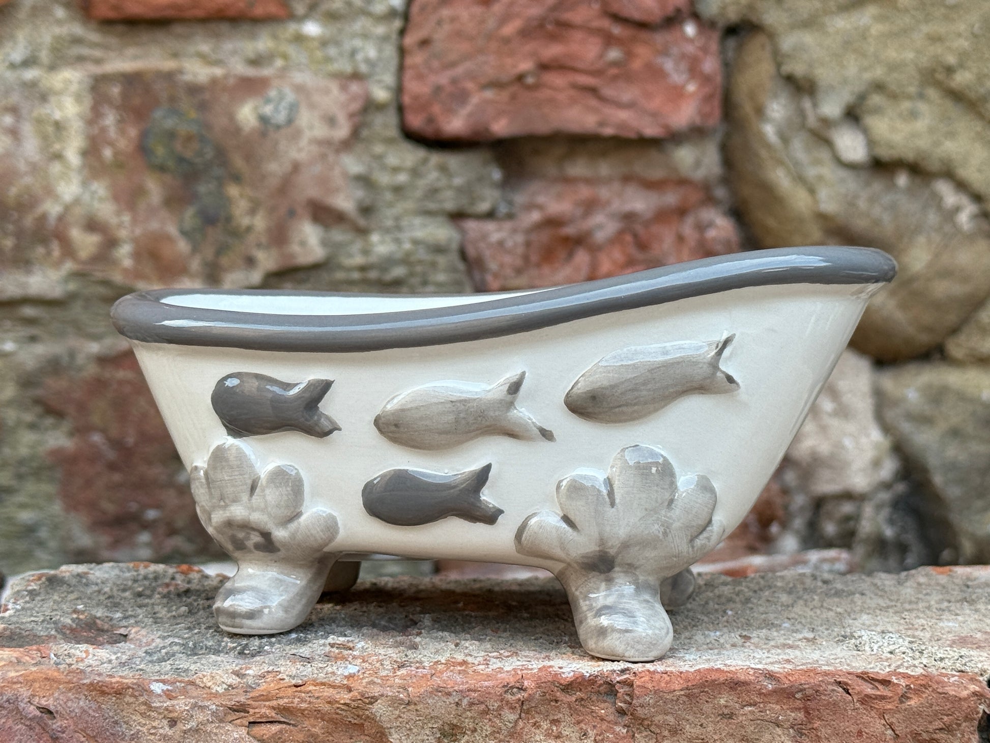 Ceramic bathtub with fish designs against a stone wall background