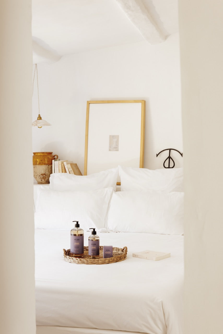 Bedroom with white bedding and a tray with bottles on a nightstand.