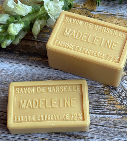 Two bars of Madeleine Marseille soap on a wooden surface with a sprig of lavender.