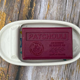 Bar of soap labeled 'Patchouli' in a white dish on a wooden surface