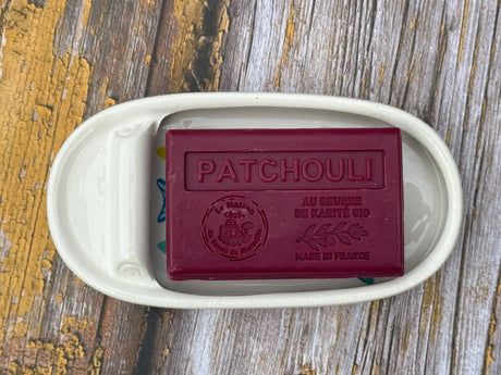 Bar of soap labeled 'Patchouli' in a white dish on a wooden surface