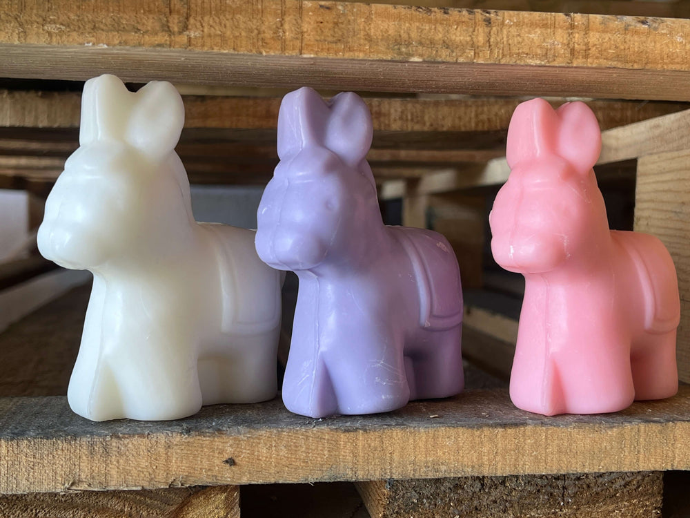 Three Donkey-shaped soap bars in white, purple, and pink on a wooden bar. French Soap UK