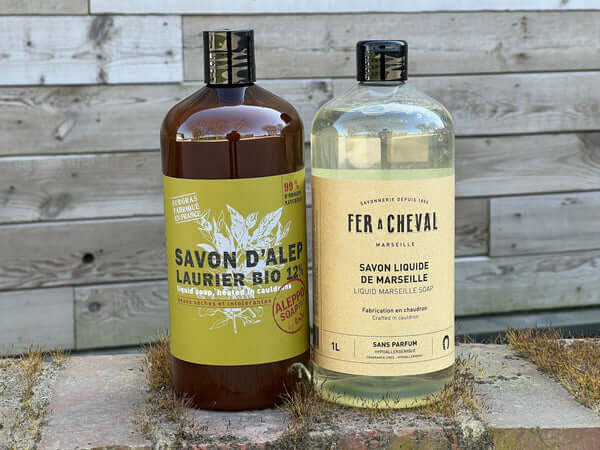 Two bottles of Savon d'Alep and Fer a Cheval soap on a wooden surface.