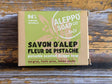 A rectangular box of Alleppo Soap Co. Savon D'Alep Pistachio Scented Allepno Soap, featuring a light green and kraft brown design, placed on a rustic wooden surface.