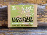 A rectangular box of Alleppo Soap Co. Savon D'Alep Pistachio Scented Allepno Soap, featuring a light green and kraft brown design, placed on a rustic wooden surface.