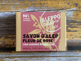 A rectangular box of Aleppo Soap Co. Rose Scented Alppio Soap, featuring a dusty rose and beige design with black and white text, placed on a rustic wooden surface.