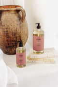 Two bottles of 'Ten Thousand Villages' soap on a white surface with a rustic vase in the background.