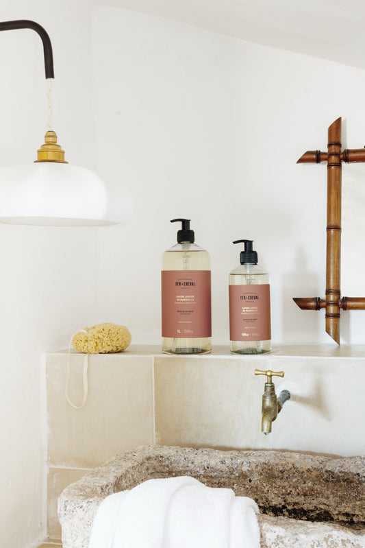 Bathroom setting with bottles on a shelf, faucet, and bath mat.
