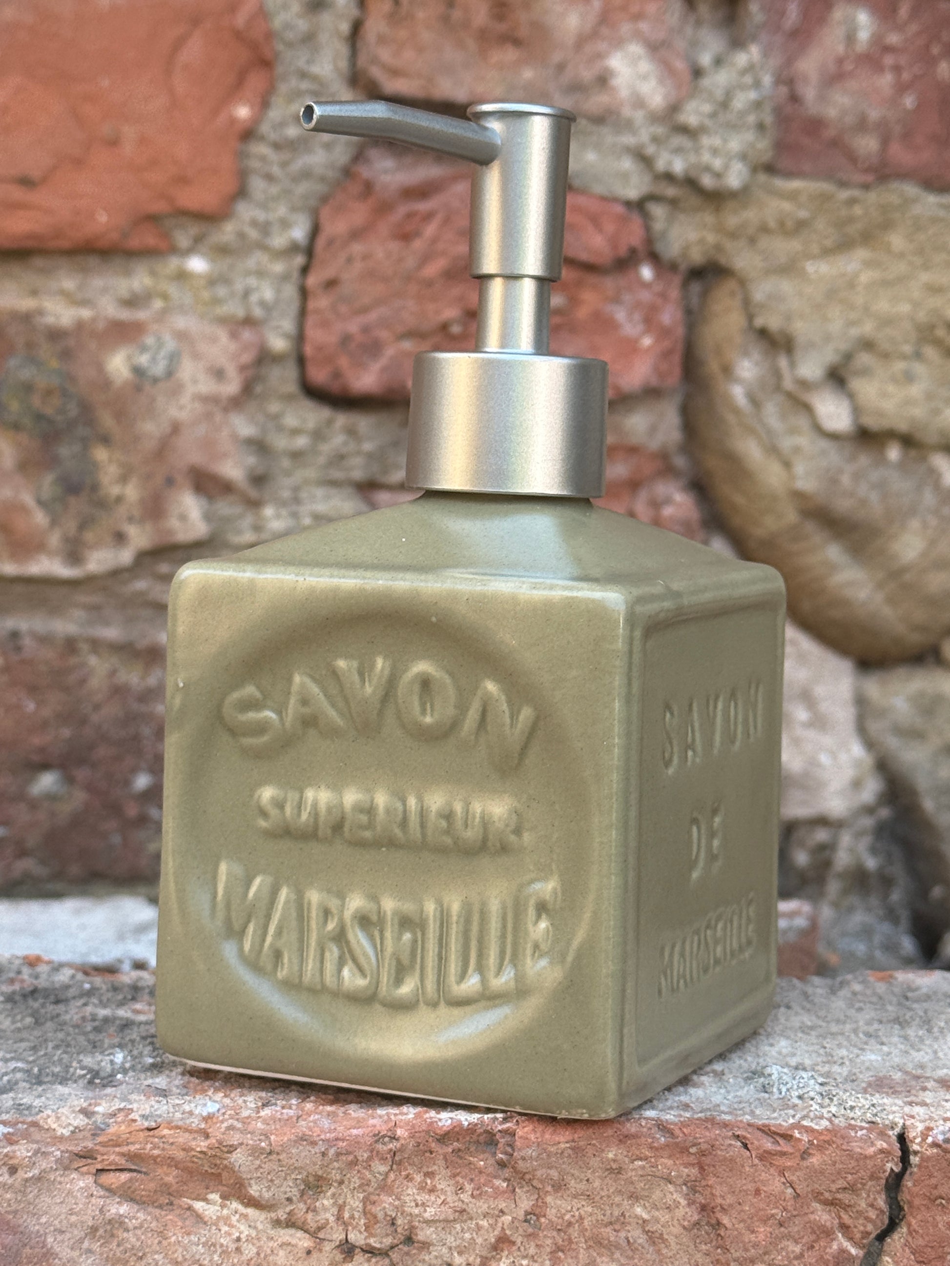 Soap dispenser with 'Savon de Marseille' branding attached to a stone wall.