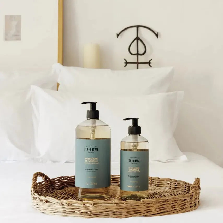 Two bottles of body wash on a tray with pillows and a candle in the background