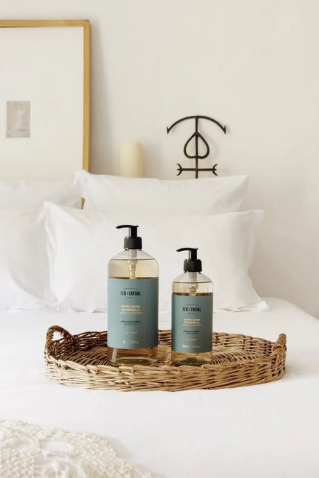 Two bottles of body wash on a tray with pillows and a candle in the background