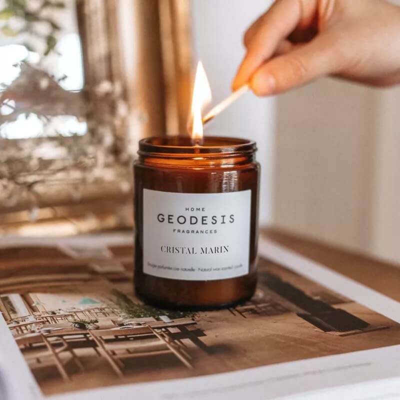 Person lighting a Geodesis candle with a match on a magazine