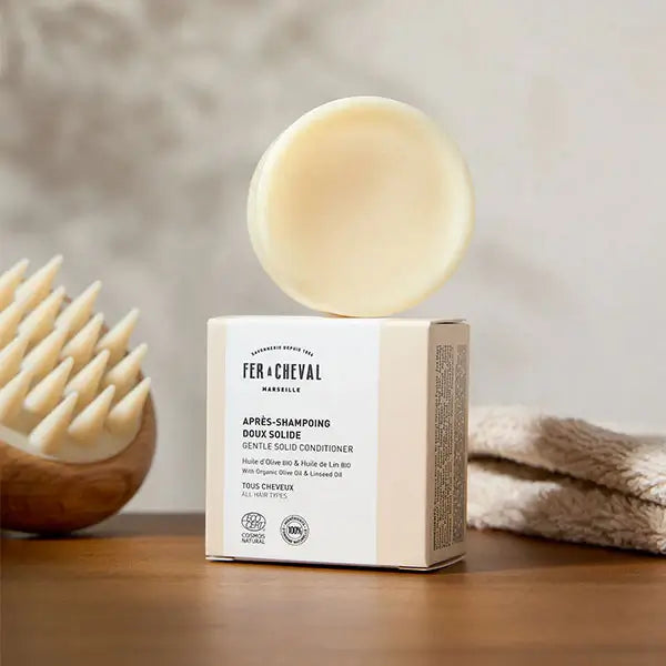 Solid shampoo bar on a box with a wooden brush and towel in the background