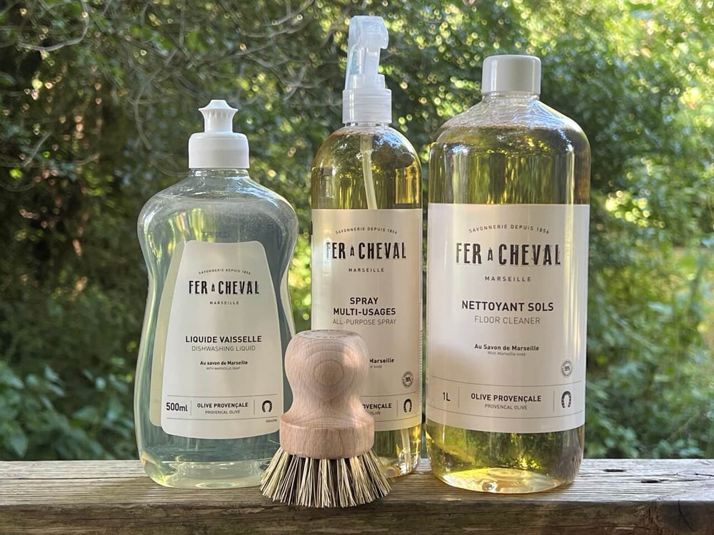 Three bottles of Fer a Cheval cleaning products on a wooden surface with a natural background.