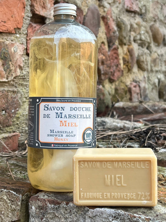 A clear plastic bottle filled with yellow liquid soap, labeled 'Savon de Marseille Miel'. Next to the bottle is a bar of soap with the same label.