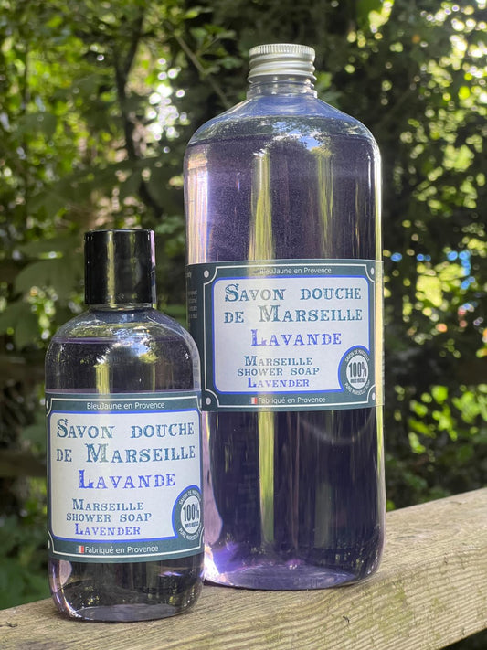 Two bottles of liquid Marseille soap with lavender fragrance, one larger and one smaller, displayed outdoors.