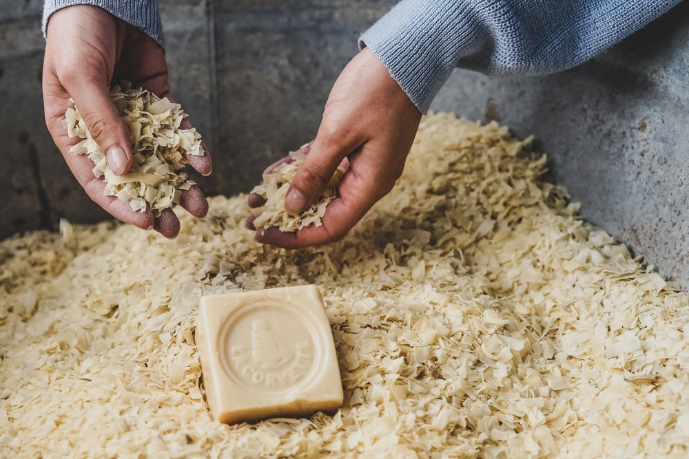 Hands holding natural soap flakes above a block of soap 