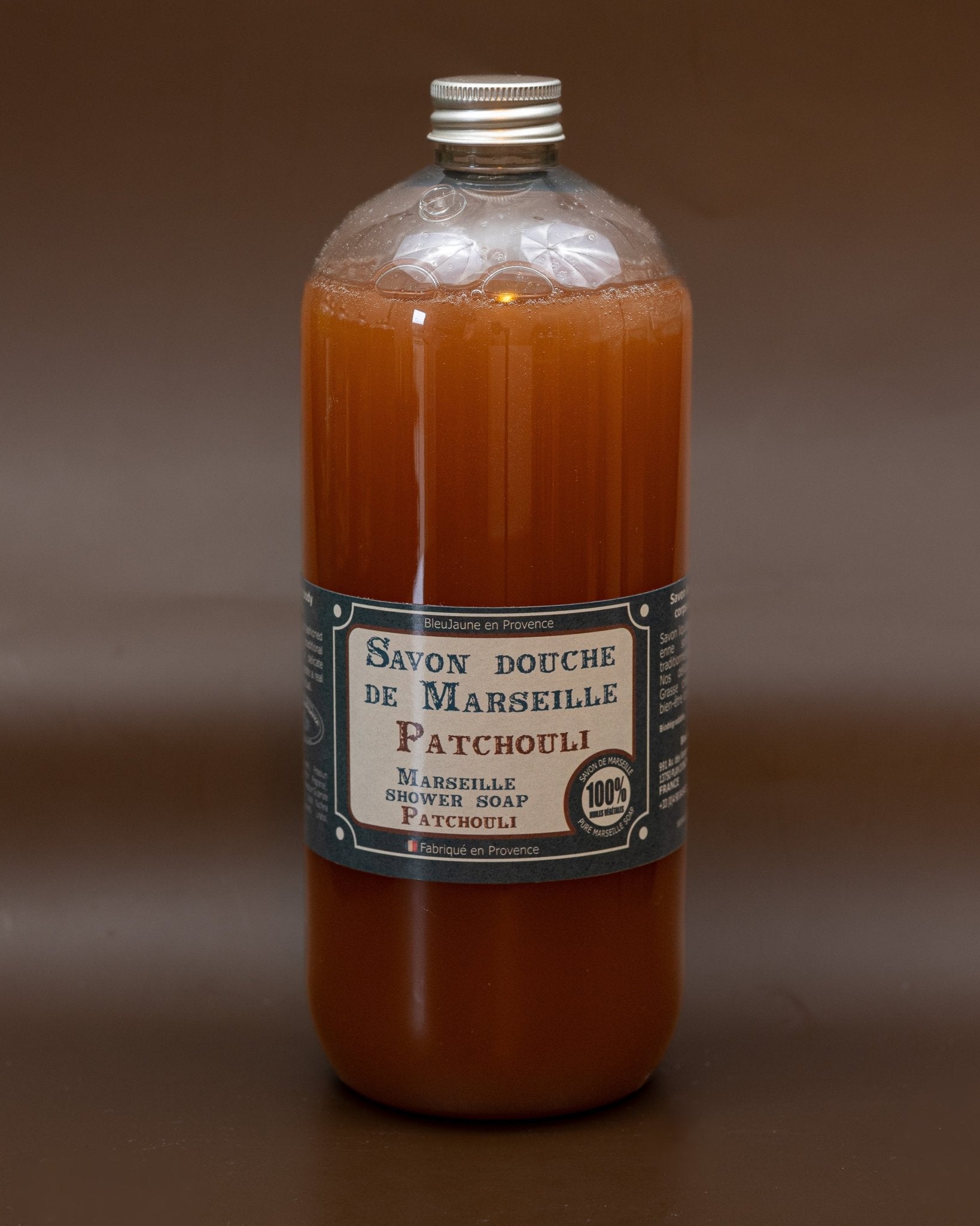 A clear plastic bottle containing orange liquid soap, labeled 'Savon bouche de Marseille Patchouli' with additional text indicating the size and fragrance.