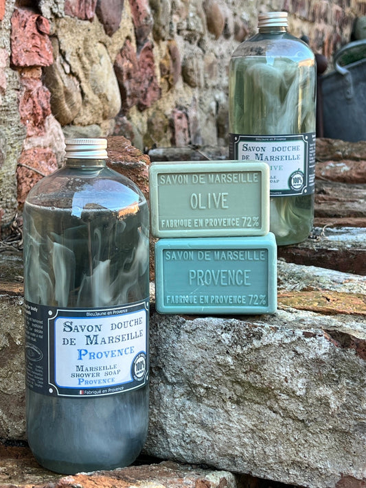 Bottle of Provence Marseille liquid soap with a green label, placed on a stone surface. Another bottle and a bar of soap are visible in the background.