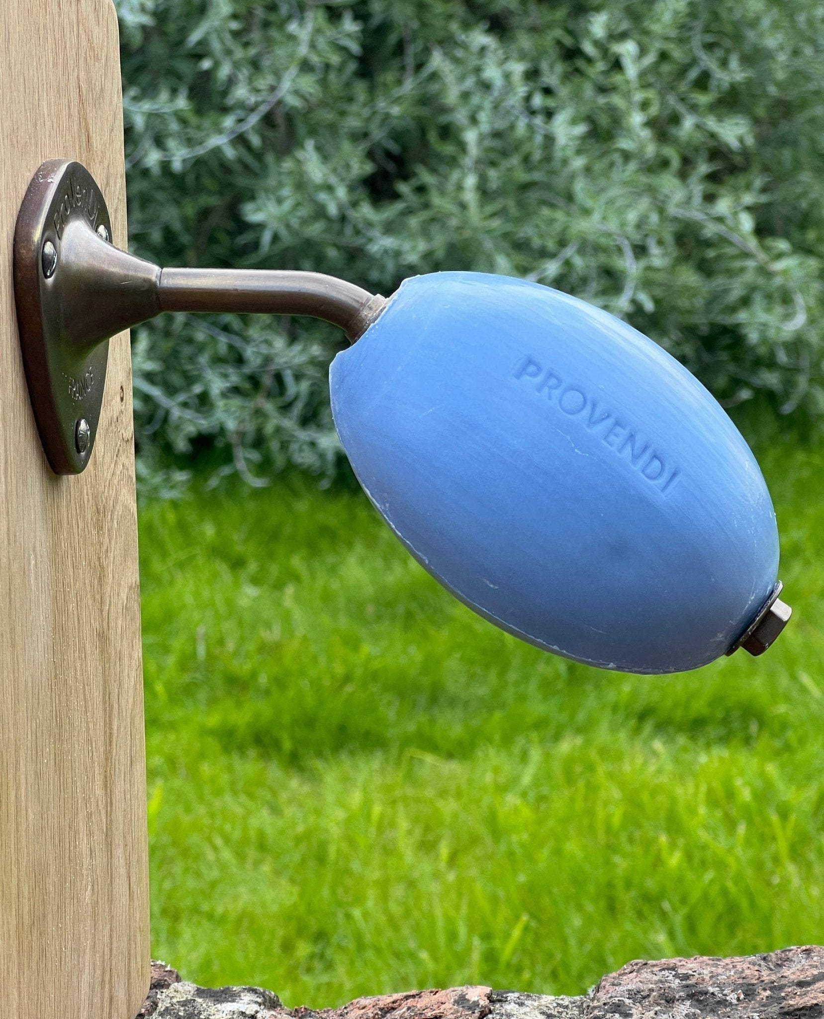 Blue Proveni product attached to a wooden post with greenery in the background