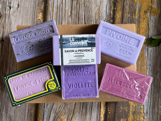 Collection of various purple coloured French soaps with labels on a wooden surface