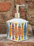 Decorative ceramic liquid soap dispenser with colourful fish design on a stone wall background