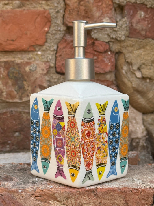 Decorative ceramic liquid soap dispenser with colourful fish design on a stone wall background