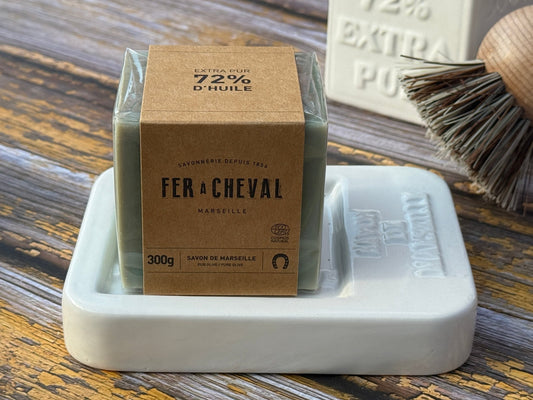 Fer a Cheval Marseille soap bar with packaging on a white soap dish on a wooden surface