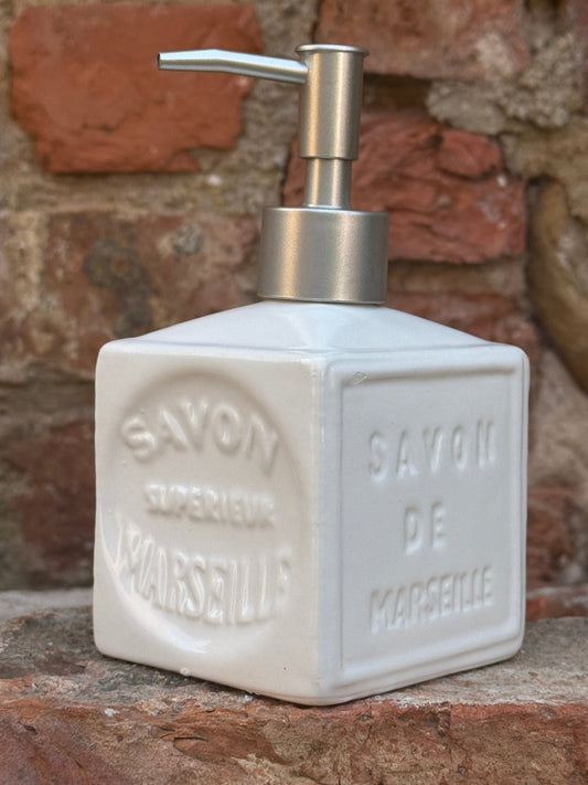 White soap dispenser with 'Savon de Marseille' text on a stone background